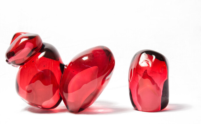 Clustered and sensuous oblong forms in translucent red glass have a smooth polished surface like the fruit that surrounds pomegranate seeds.