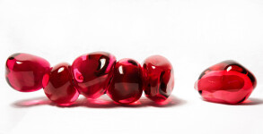 Clustered and sensuous oblong forms in translucent red glass have a smooth polished surface like the fruit that surrounds pomegranate seeds. Image 6