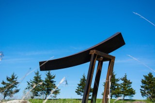 Corten steel shaped into a curved orthogonal is held, obliquely by narrow verticals in this dynamic sculpture by Claude Millette.