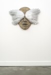 This contemporary wall sculpture is a mask forged from metal adorned with the wings of a bird. Image 3