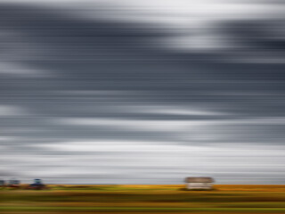 A long, flat strip of golden brown and green land dotted with outbuildings below a vast sky captures the essence of the Canadian prairie.