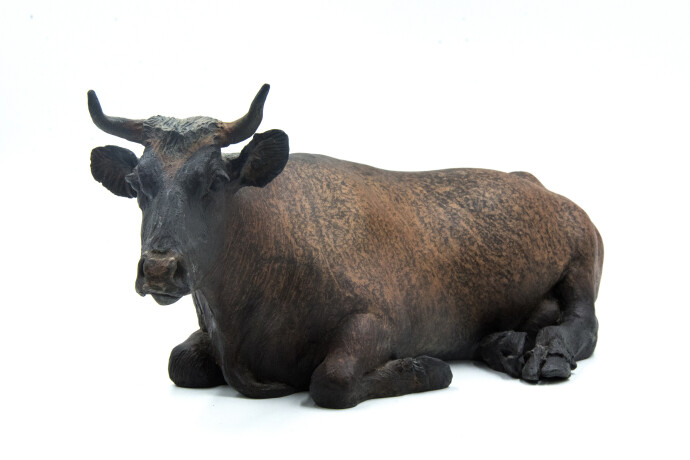 Jeanette is a table-top sculpture of a regal adult female cow sitting, legs tucked under her massive body.