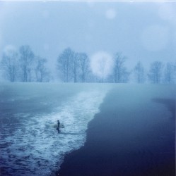 In this moody, magical photo by Mark Bartkiw a lone surfer, board tucked under one arm wades into the sea.