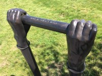 Like long arms, two vertical copper pipes topped by bronze cast hands emerge from the ground in this outdoor sculpture. Image 4