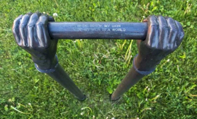 Like long arms, two vertical copper pipes topped by bronze cast hands emerge from the ground in this outdoor sculpture.