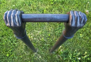 Like long arms, two vertical copper pipes topped by bronze cast hands emerge from the ground.