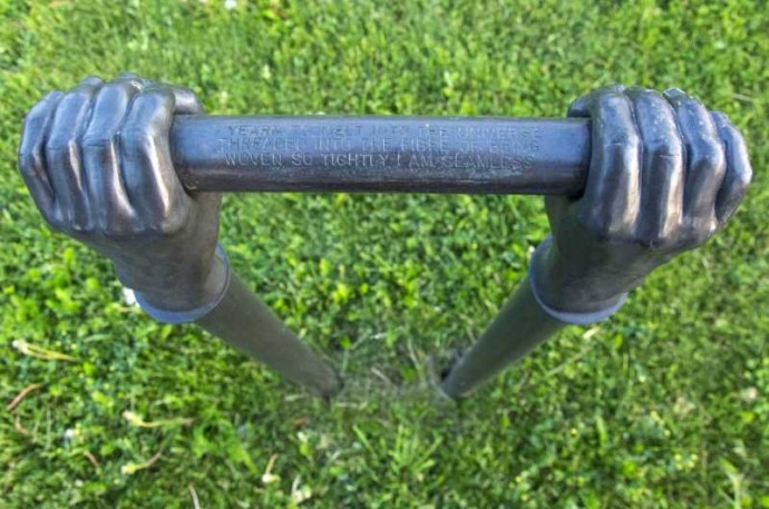 Like long arms, two vertical copper pipes topped by bronze cast hands emerge from the ground.