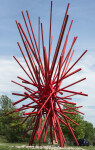 In an explosion of colour bright red painted steel poles crisscross one another in this dynamic abstract sculpture by Shayne Dark. Image 4