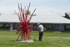 In an explosion of colour bright red painted steel poles crisscross one another in this dynamic abstract sculpture by Shayne Dark. Image 5